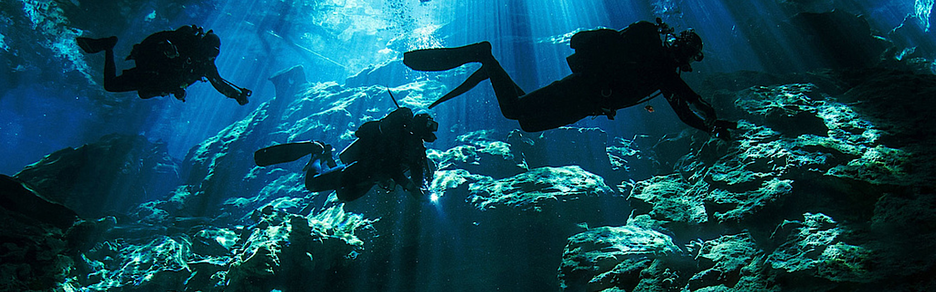 Scuba-Taucher erkunden eine Unterwasserhöhle mit eindrucksvollen Lichtstrahlen, die durch das Wasser brechen.