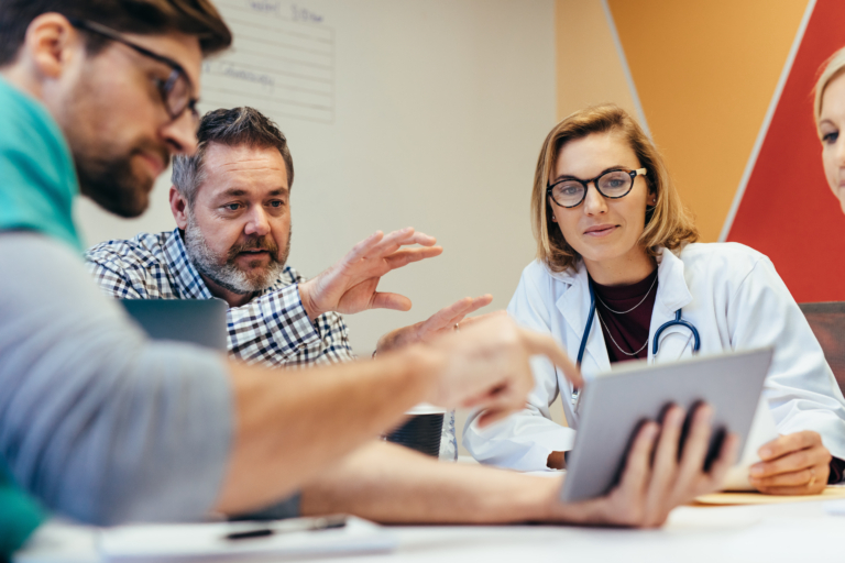 Drei Personen in einem Meeting, eine Ärztin mit Tablet berät mit Kollegen bei ADEX Partners.