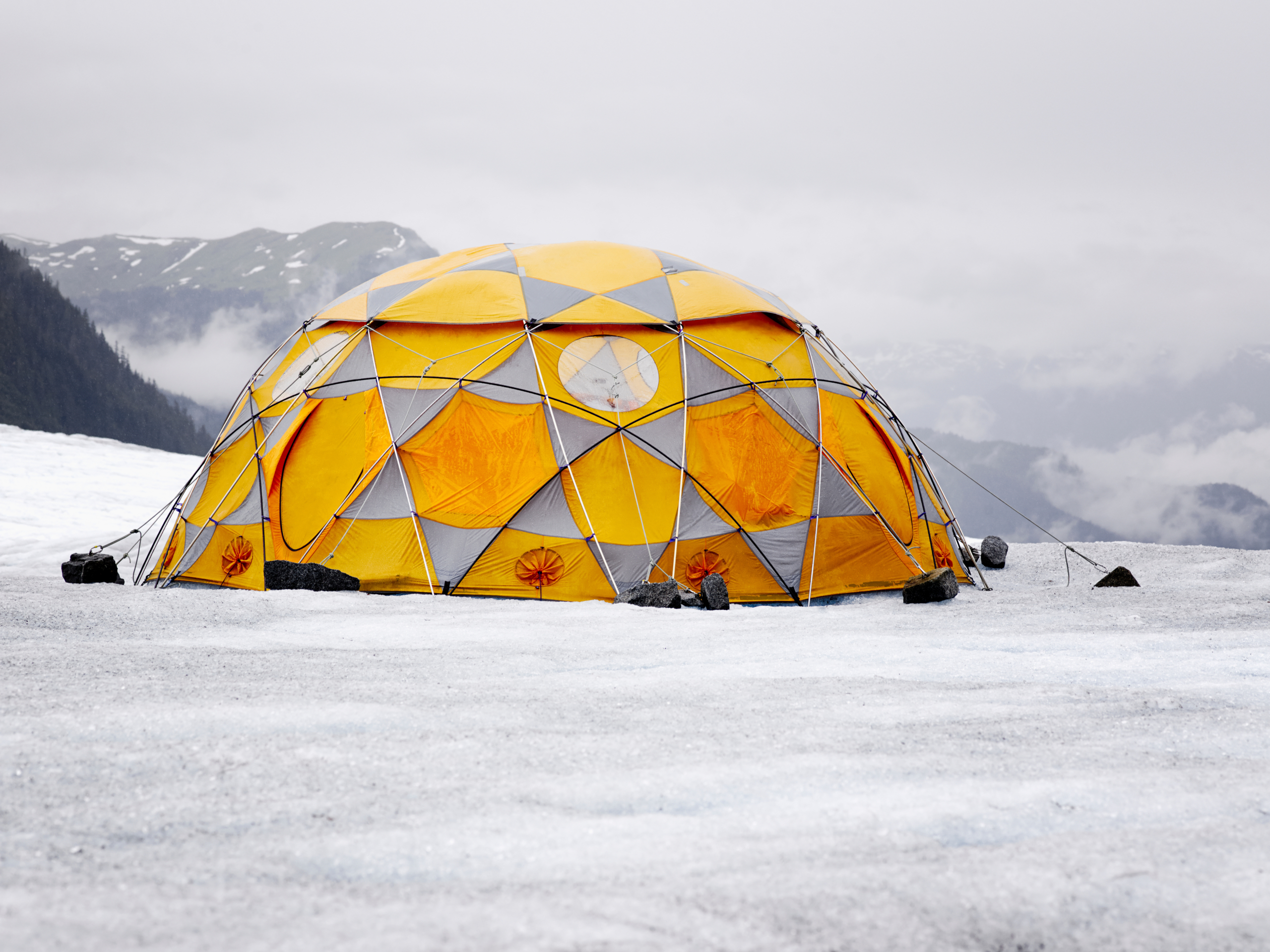 Geodätische Kuppelzelt auf verschneiter Oberfläche mit nebligen Bergkulissen im Hintergrund.