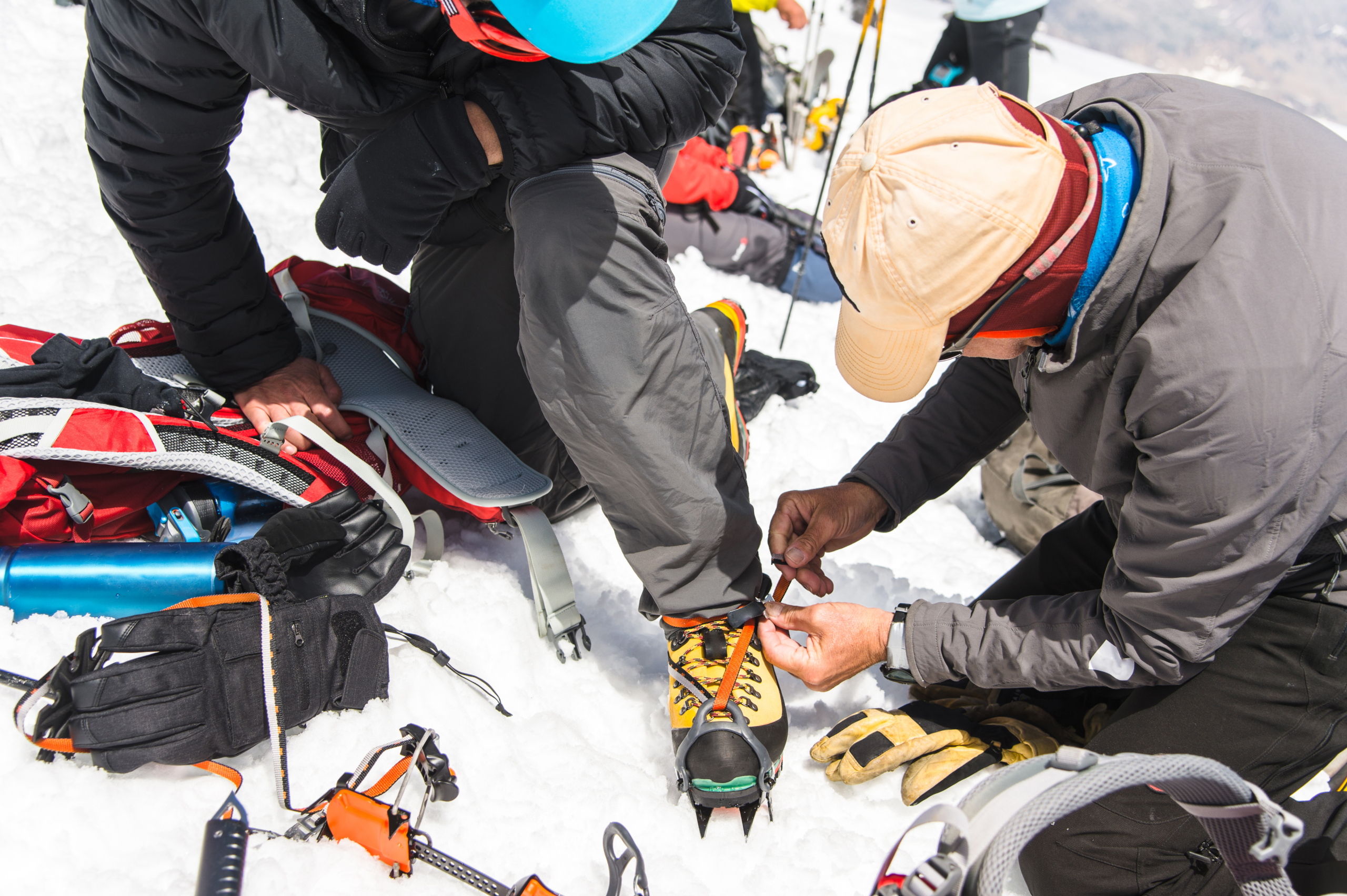 Zwei Bergsteiger binden im Schnee professionelle Kletterschuhe mit Steigeisen.