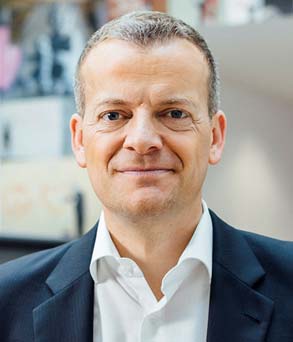 Geschäftsmann mit Anzug und offenen Hemdkragen lächelt freundlich, Porträtaufnahme.