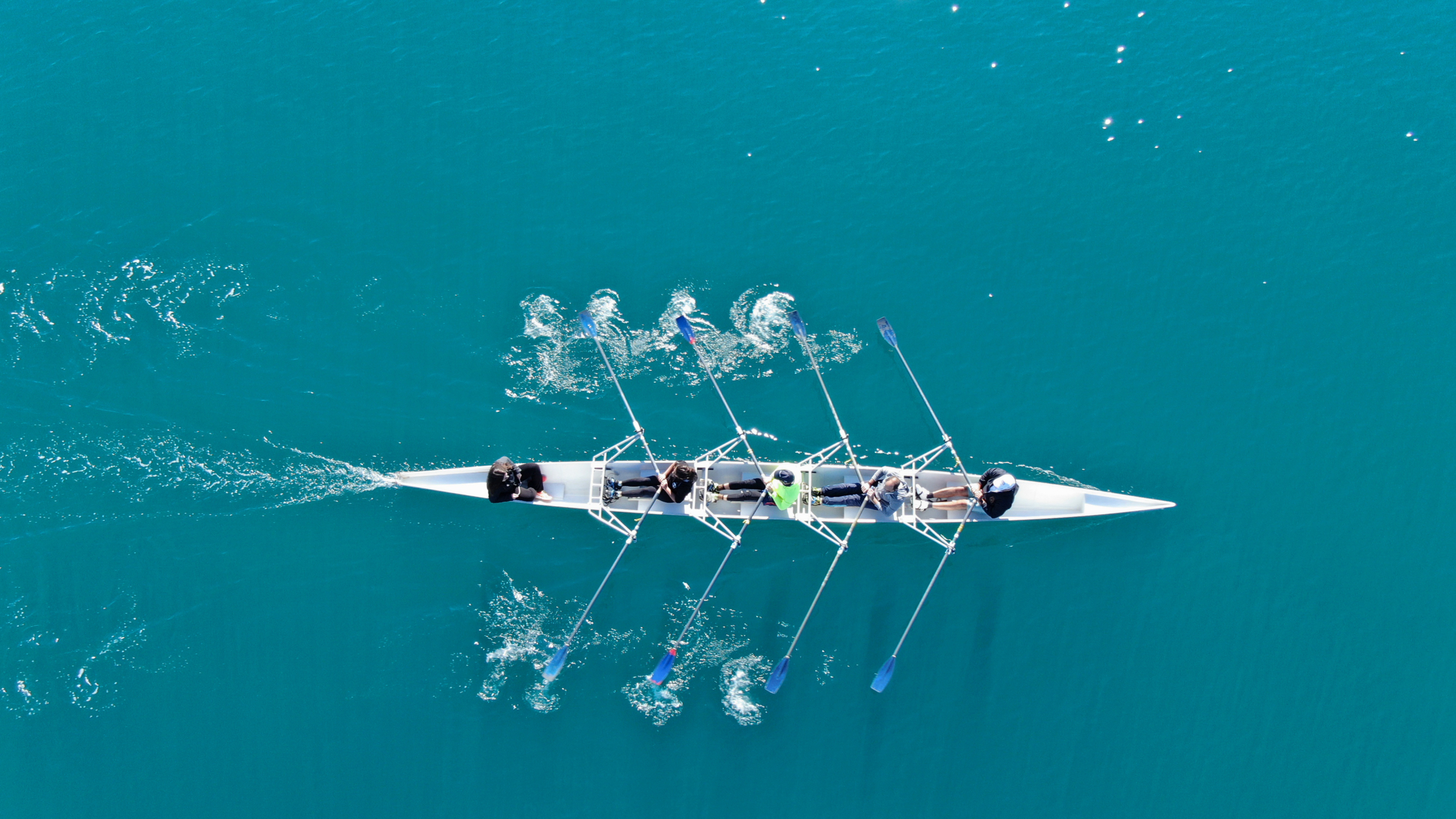 Rowing team on blue water from above.