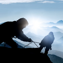 Climbers silhouetted against sunrise in mountains.