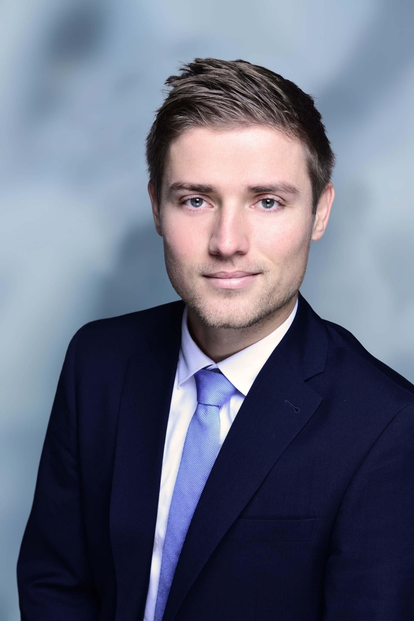 Professionelles Porträt von Sören Hallmann in blauem Anzug und hellblauem Hemd vor unscharfem Hintergrund.